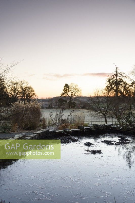 View across an icy pond on a January morning into the surrounding Herefordshire landscape at Hergest Croft