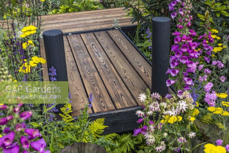 Charred wooden boardwalk set among flowering perennials. June

