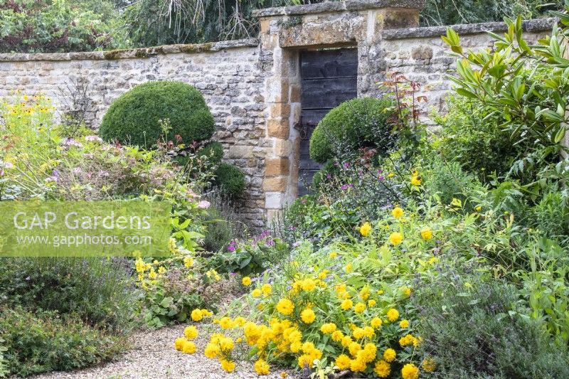 Perennials spill onto a gravel path that leads to a door set into a stone wall at The Manor, Little Compton.
