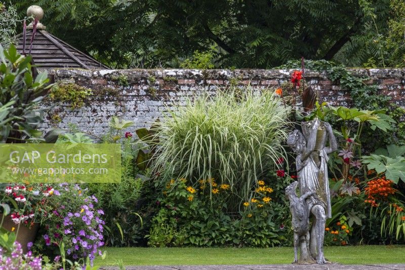 A statue stands in front of mixed planting in the Swimming Pool Garden borders with grasses, cannas and perennials.