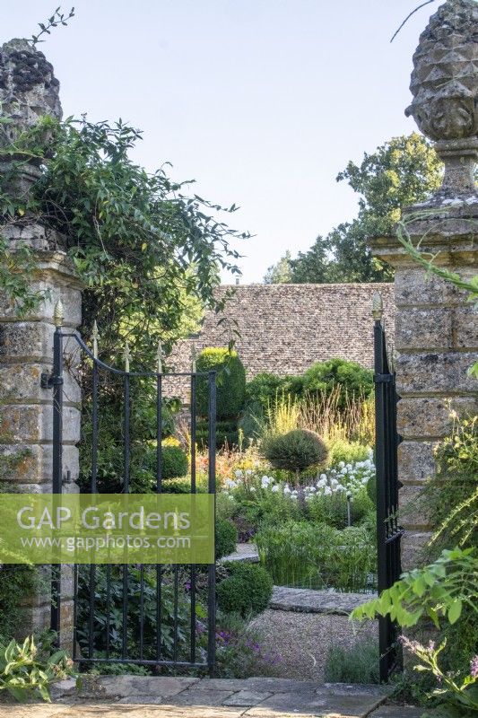 Looking through wrought iron gates set into stone pillars into The Flower Garden at The Manor, Little Compton.