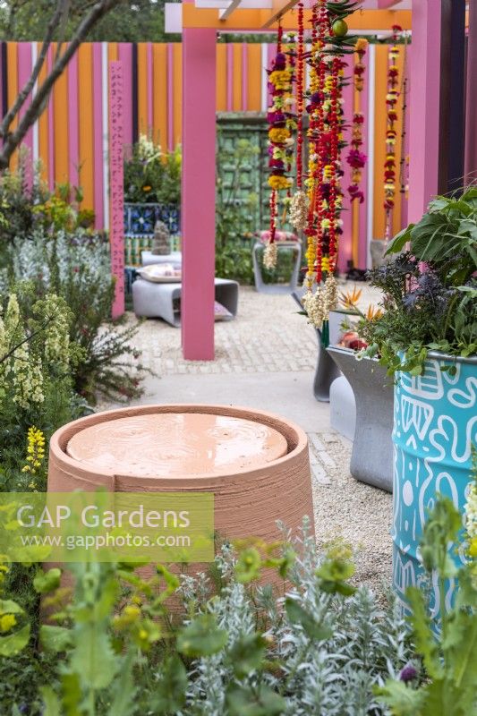 Pastel pink circular water feature next to painted oil drum. The RHS and Eastern Eye unity garden. Designer: Manoj Malde