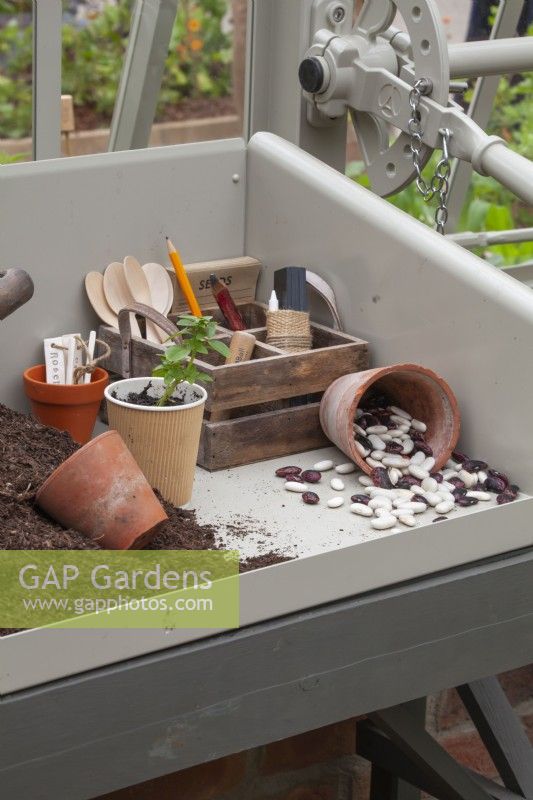 Potting bench with garden tools, compost and  bean seeds in a clay pot.