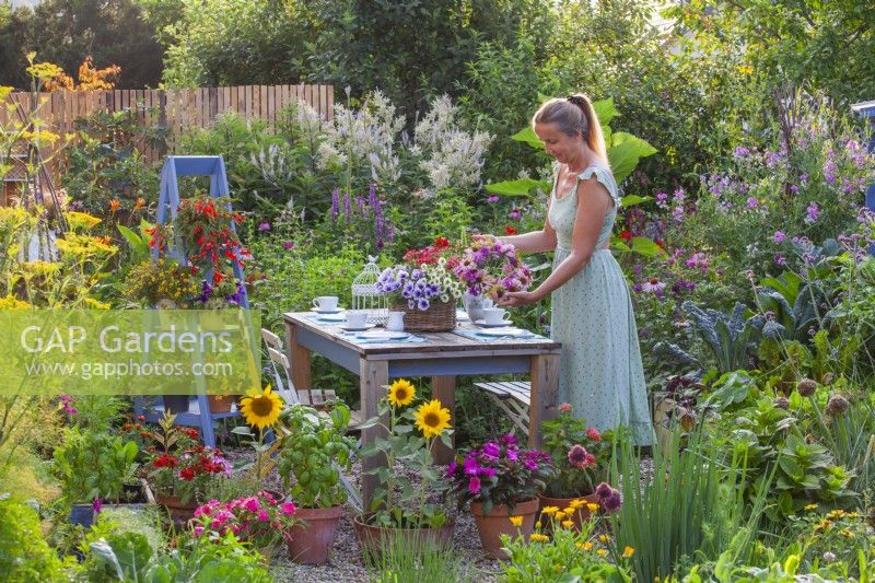 A woman adds a wreath made of summer flowers to a table ready for tea.