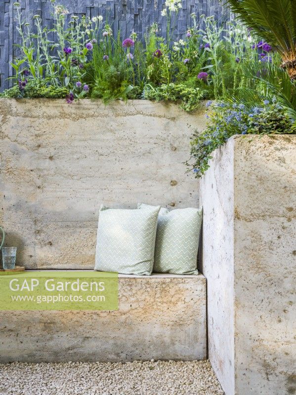 Inbuilt seating made with two cushions. Seating and a wall made of hypertufa in concrete style. The Shifting Garden, Designer: The Chelsea Gardener, RHS Chelsea Flower Show 2023