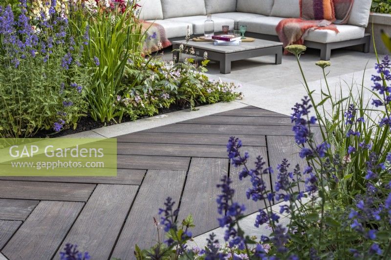 A boardwalk leading to the patio made of wood imitation material and surrounded by a perennial bed planted with Nepeta. June. Designer: Kevin Dennis 