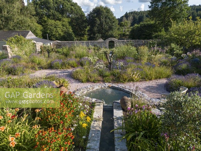 Rill and pond in summer walled garden, informal planting of drought tolerant plants in gravel