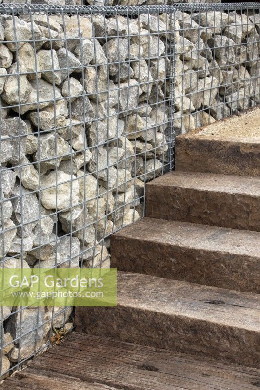 Gabions filled with stone offcuts form a wall next to steps made from reclaimed wood - designers Caroline and Peter Clayton - Get Started Gardens -  Nurturing Nature in the City -  RHS Hampton Court Palace Garden Festival.