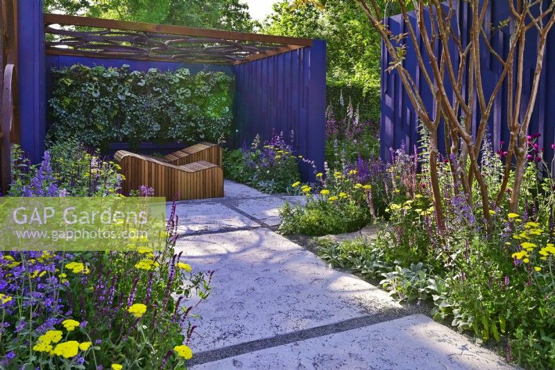 Garden space surrounded by a navy blue painted panels with path with an original leaves design and relaxation area with decorative wooden deckchairs set against living green wall under openwork of pergola roof. Planting includes: Achillea millefolium 'Moonshine', Nepeta faassenii 'Junior Walker, Salvias nemorosa 'Caradonna Pink', 'Amethyst' and  multi-stem Lagerstroemia indica. June
Bord Bia Bloom, Dublin
Designer: Jane McCorkell
