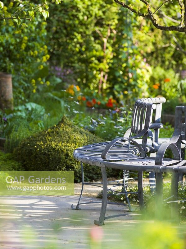 A metal tree seat in the Savills Garden, Designer: Mark Gregory, RHS Chelsea Flower Show 2023, May, Spring, Summer
