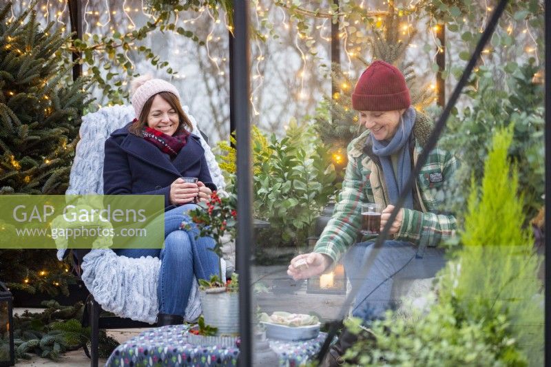 Women sitting in greenhouse with hot drinks