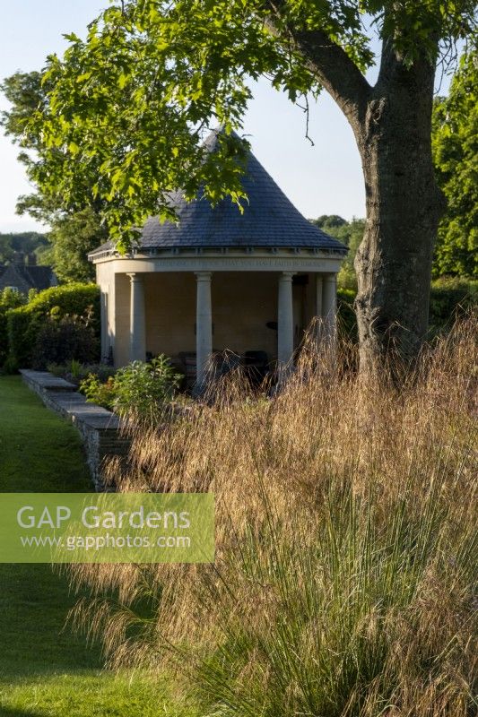 Temple style summerhouse in summer garden with Stipa gigantea, Giant Oat Grass