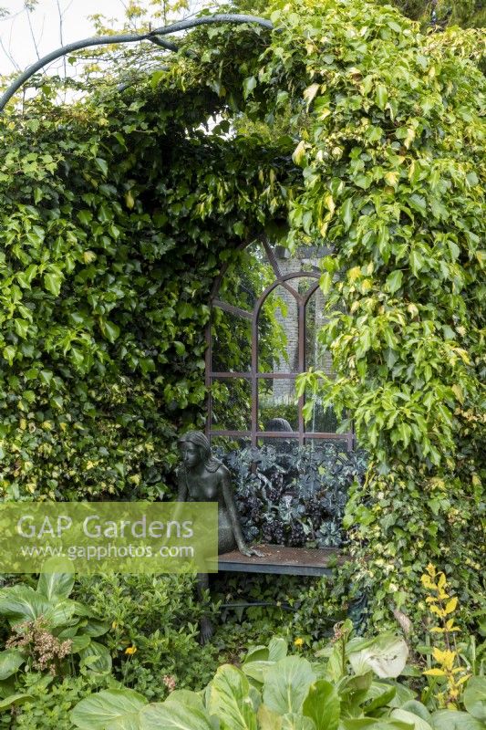 An ivy covered arbour with mirrored backdrop and statue of a young girl.