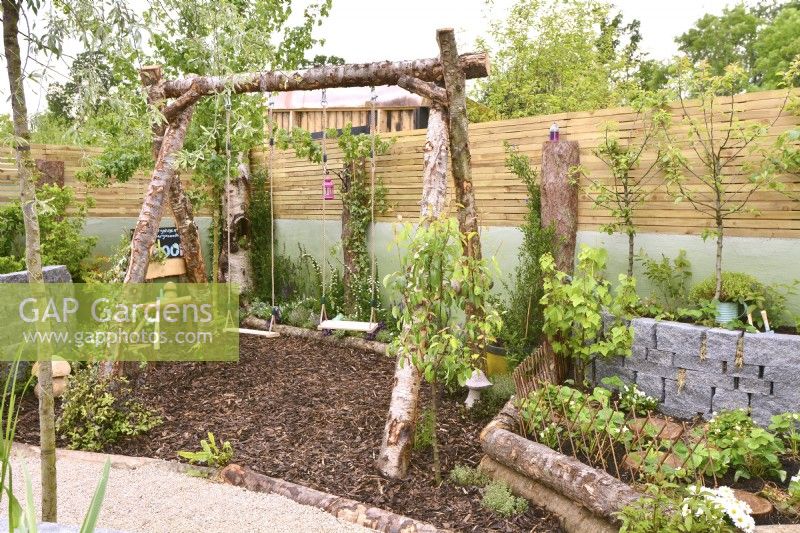 Childrens play area with swing made of raw birch trunks. Strawberry bed. Planted with Pyrus in a woodland inspired garden surrounded by a wooden planks fence. June
Designer: Mary Anne Farenden. Bord Bia Bloom, Super Garden, Dublin, Ireland.