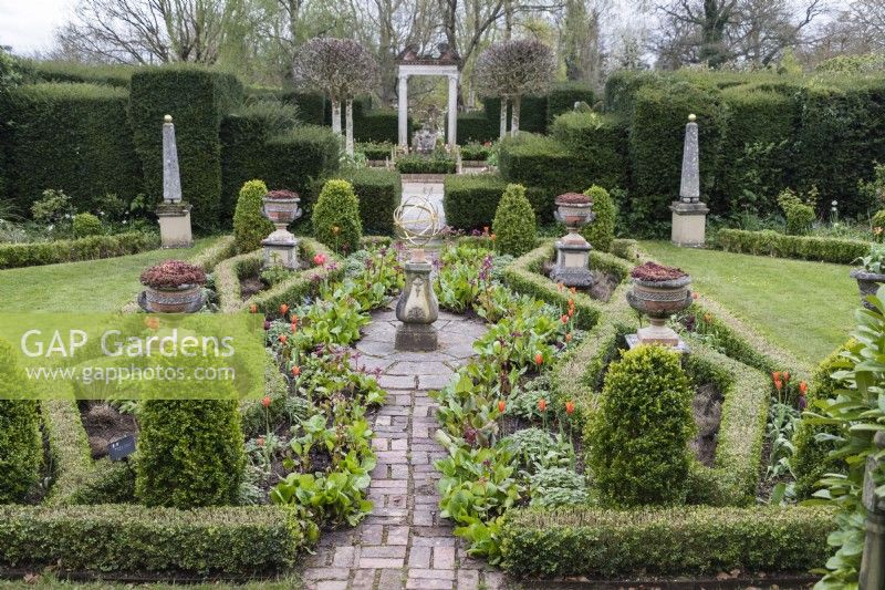 The Silver Jubilee Garden with borders planted with tulips and low hedge of Box. Armillary in centre. Obelisks on plinths. April. Spring. 