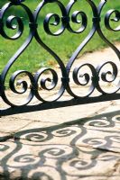 Shadows on a path from an ornate painted gate at Barnsley House, Gloucestershire.