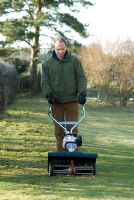 Man removing moss and thatch from the grass with a petrol powered scarifyer in March