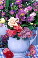 Late summer floral arrangement in blue jug - roses, hibiscus, asters, godetia and gentian