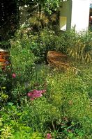 These Four Walls Garden at Chelsea Flower Show 2006 with bent wooden bench made from steamed Oak and Birch ply from New Zealand in woodland with planting of Stipa gigantea, Astrantia and Thalictrum - Thick wall with window in background 