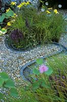 Time Line Garden at Hampton Court Flower Show 2006 designed by Emma Dawson from Capel Manor College - Erigeron karvinskianus, Salvia nemorosa 'Ostfriesland' Hemerocallis, Cosmos and Stipa arundinacea by meandering beaten lead stream course with pebble patio and pebble gabion wall 