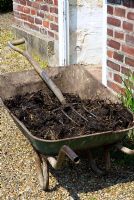 Wheelbarrow of muck with fork ready for vegetable garden outside greenhouse