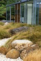 Garden view with boulders and native grasses contrasting with modern building at Piha, New Zealand. Garden Design - Ted Smyth. 