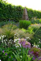 Mixed border early June, including Allium christophii, double Aquilegias, Geraniums and Delphiniums with wooden obelisk and pleached lime hedge