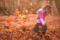Little girl kicking autumn leaves