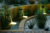 Gravel garden with water rill, rendered concrete walls and three spouts lit up at night