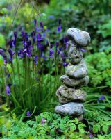 Sculpture made from a pile of stones with Hyacinthoides non-scripta - bluebells in background 