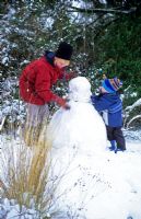 Mother and child making snowman in garden
