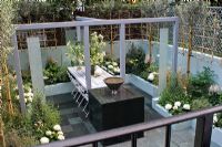 Grey steel painted frame supporting marble 'floating' table. Courtyard - 'enteraining' garden in whites, purple and green. Trellis with Olive trees trained in fan shape for privacy