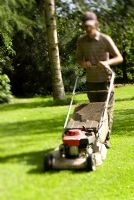 Man cutting grass lawn with petrol driven rotary lawnmower