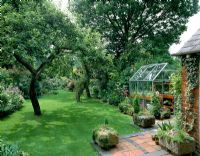 View down garden from back of house, with well-kept lawn and small greenhouse on left  