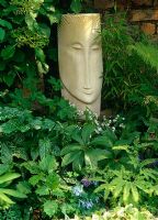 Sculpture by Wendy Marshall, in shady area with Pulmonaria 'Opal', Ajuga incisa, Corydalis flexuosa 'Pere Davide', Hellebore, fern foliage and Arum italicum 'Pictum'