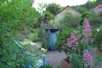 Seating area with contemporary water feature within borders. Selfseeded valerian in gravel