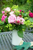 Roses and achemilla mollis in white jug on garden table with gloves
