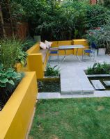 Aluminium table and chairs on patio surrounded by yellow rendered walls with raised beds and rill. Oleander in galvanised container. 