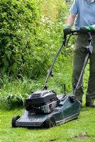 Man mowing the lawn with a petrol driven rotary mower in spring