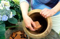 Woman placing broken pieces of teracotta into a pot for drainage