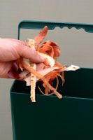 Vegetable peelings being added to kitchen waste bin for composting