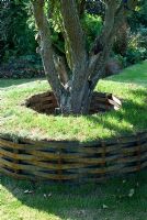 Turf tree seat with strips of metal woven around tubes that have been allowed to rust - beneath an old apple tree