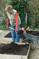 Woman applying organic compost from wheelbarrow on to raised beds