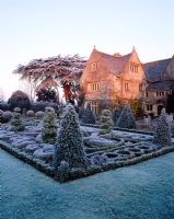 View across the frosted celtic knot garden with topiary, towards the sunlit house - The Abbey House, Wiltshire