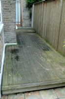 Area of decking at the side of a terraced town house in need of a clean. Ring marks show where containers have been placed and darker areas show algae build-up.