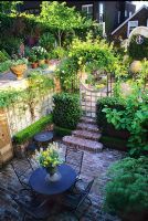 Overview of urban courtyard garden with brick paved terrace with table and chairs.  
Steps and arched gateway to raised patios - San Francisco, California, USA    

