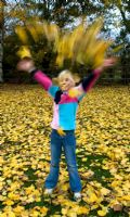 Girl throwing autumn leaves in garden - Pannells Ash Farm West Essex