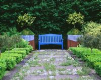 Blue bench with lead and rusty metal containers beside, planted with holly and box - Ridler's Garden, Swansea, Wales
