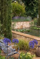 Seating area overlooking raised pond with water feature and Agapanthus africanus in foreground - The Dorset Water Lily Garden, RHS Hampton Court Flower Show 2008