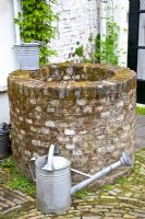 Old brick well with galvanised bucket and watering can
